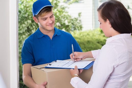 Livreur remettant un colis à une cliente, qui signe un document à la porte.