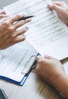 Deux mains tenant des documents et un stylo sur une table en bois.