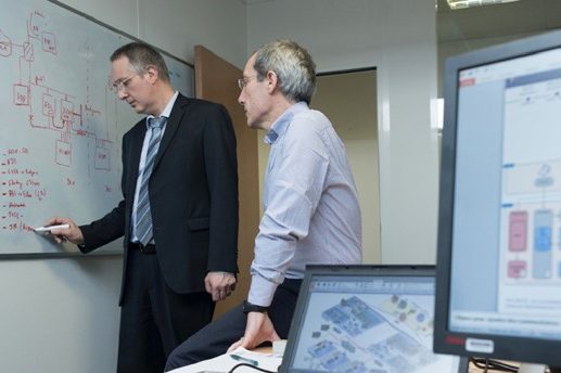 Deux hommes en costume discutent devant un tableau blanc dans un bureau.