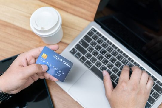 Une main tenant une carte de crédit près d'un ordinateur portable sur une table.